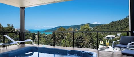 A balcony with a hot tub, outdoor seating, and a scenic view of a coastline.