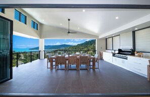 A spacious balcony with a dining table and chairs, a ceiling fan, and a view of a mountainous landscape. - Airlie Nights (Airlie Beach)