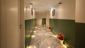 Un couloir doté d’un sol en marbre, de murs verts et blancs, et agrémenté de plantes en pot.