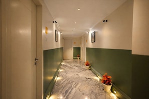 A hallway with marble flooring, green and white walls, and potted plants. - Phoenix Unmatched Comfort - Hotel Near Fateh Sagar Lake Udaipur (Udaipur)