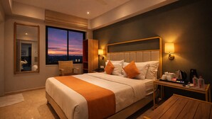 Une chambre d’hôtel moderne avec un grand lit, une table de chevet, une chaise et une vue sur la ville au coucher du soleil.