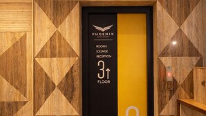 Un ascenseur d’hôtel avec un mur décoré de motifs géométriques, une signalétique indiquant que les salons et la réception se trouvent au troisième étage, et un bouton d’ascenseur orné du symbole « G ».