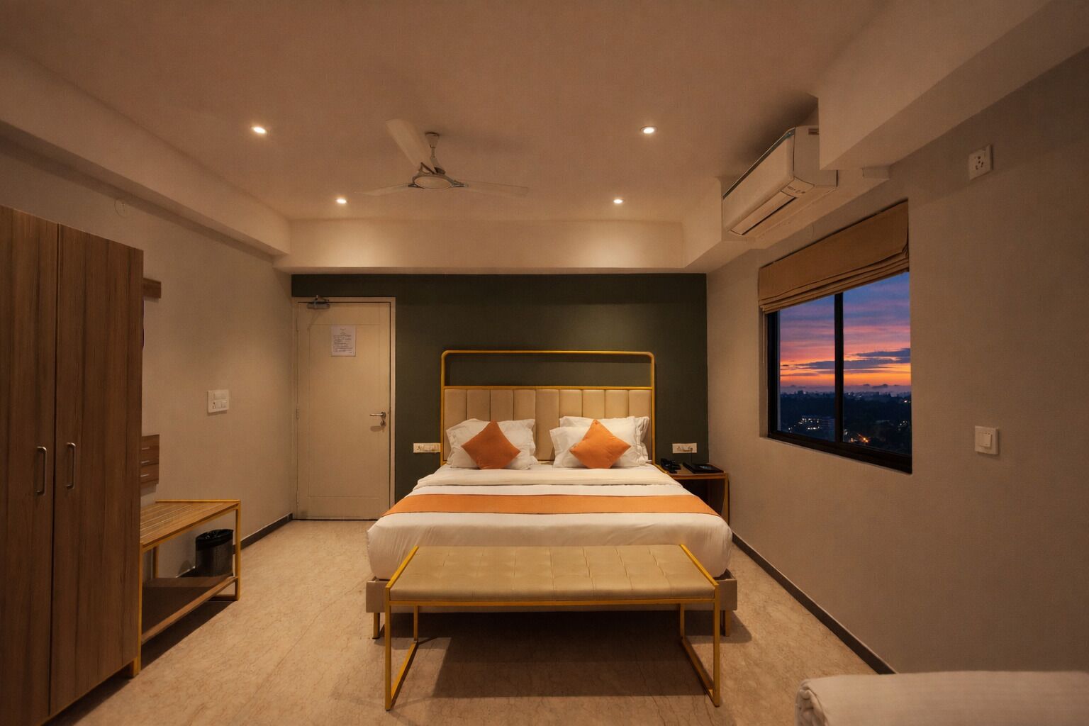 A modern bedroom with a bed, bedside table, and a view of the city at sunset.