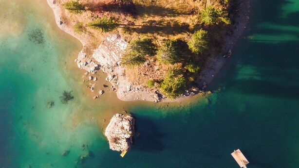 An aerial view of a small island with clear turquoise waters, rocky terrain, and sparse vegetation.
