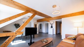 A spacious loft with exposed wooden beams, a modern sofa, a flat-screen TV, and a dining area with a table and chairs.