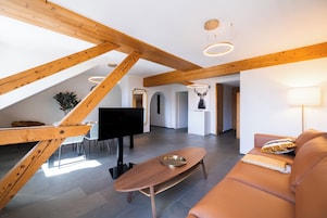 Un loft amplio con vigas de madera a la vista, un sofá moderno, un televisor de pantalla plana y un comedor con mesa y sillas.