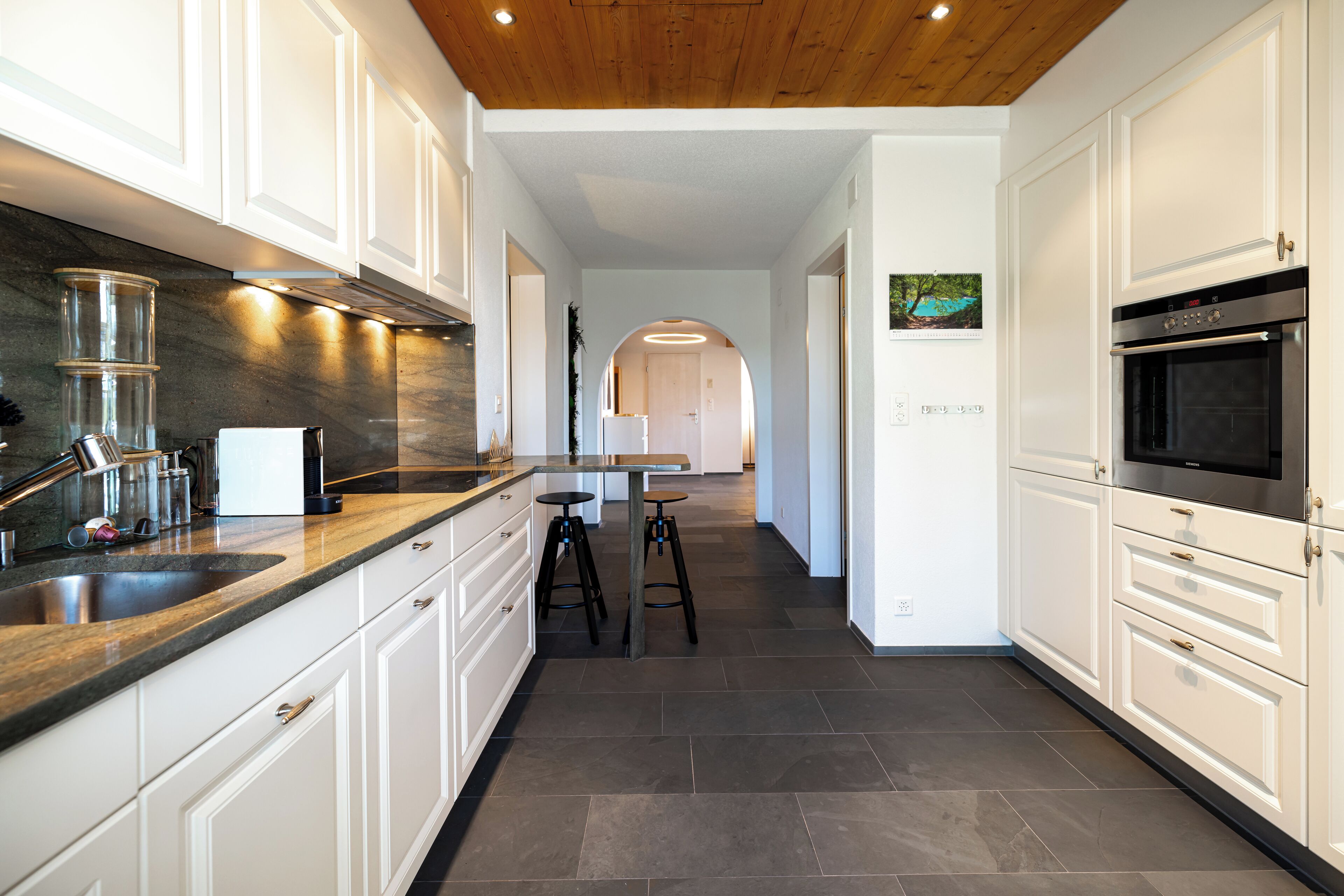 Eine moderne Küche mit weißen Schränken, einer Arbeitsplatte aus Granit und einem eingebauten Backofen.