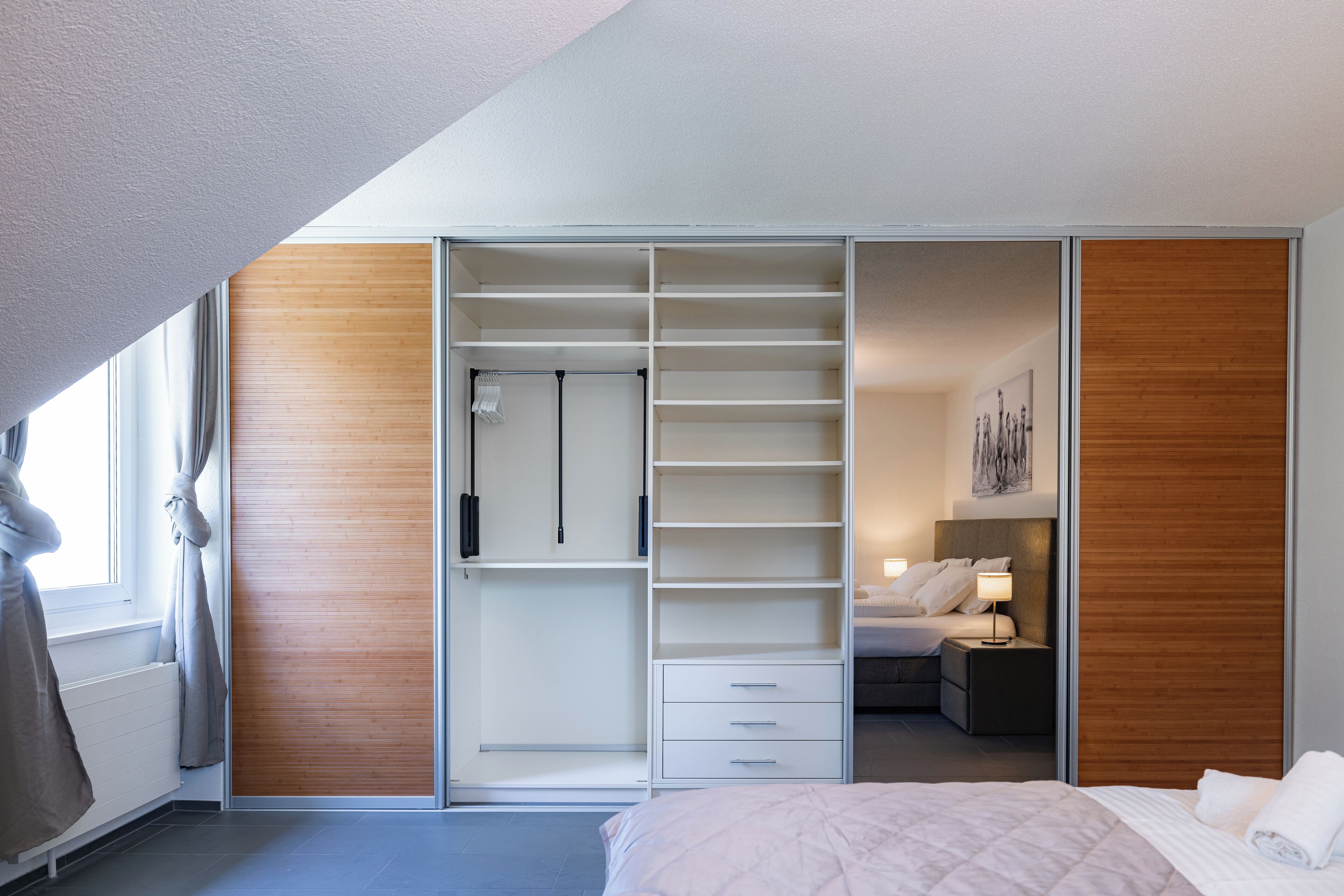 A modern hotel room with a large wardrobe, a bed, and a nightstand.