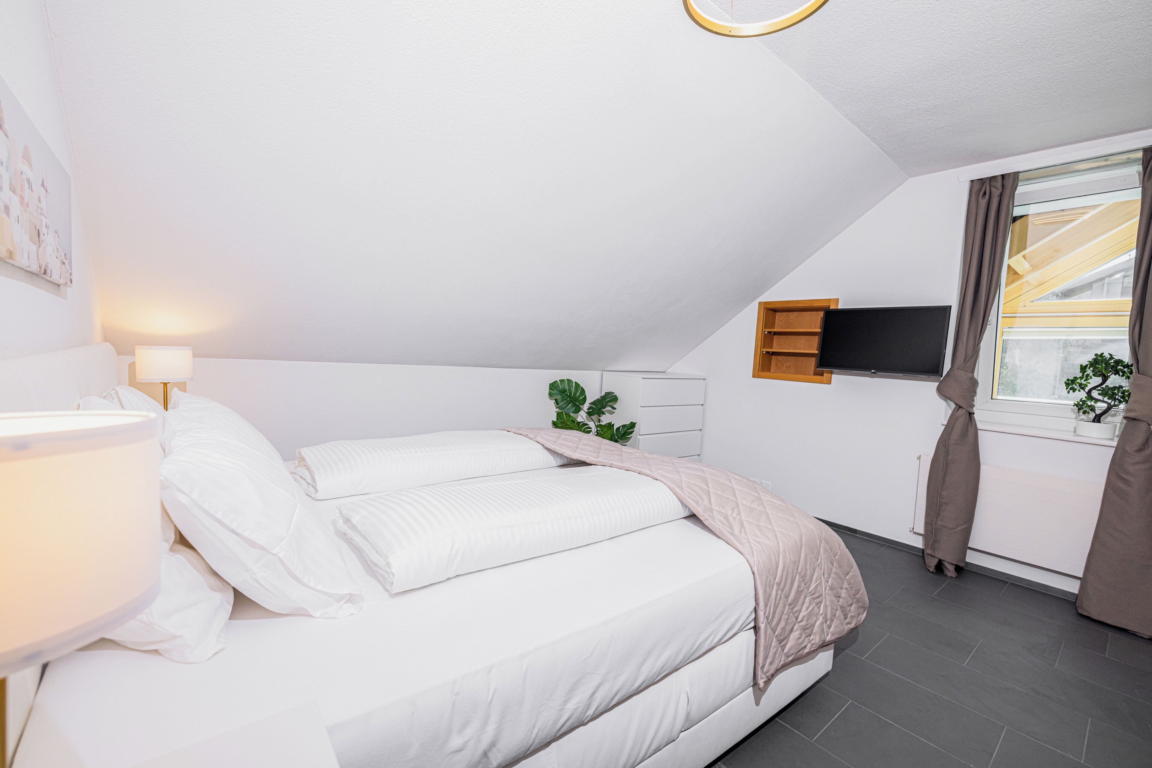 Une chambre à coucher moderne avec un lit, une lampe de chevet, un téléviseur et une fenêtre avec des rideaux.