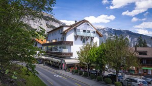 A hotel with a mountain backdrop, featuring a prominent glass facade and a traditional sloped roof.