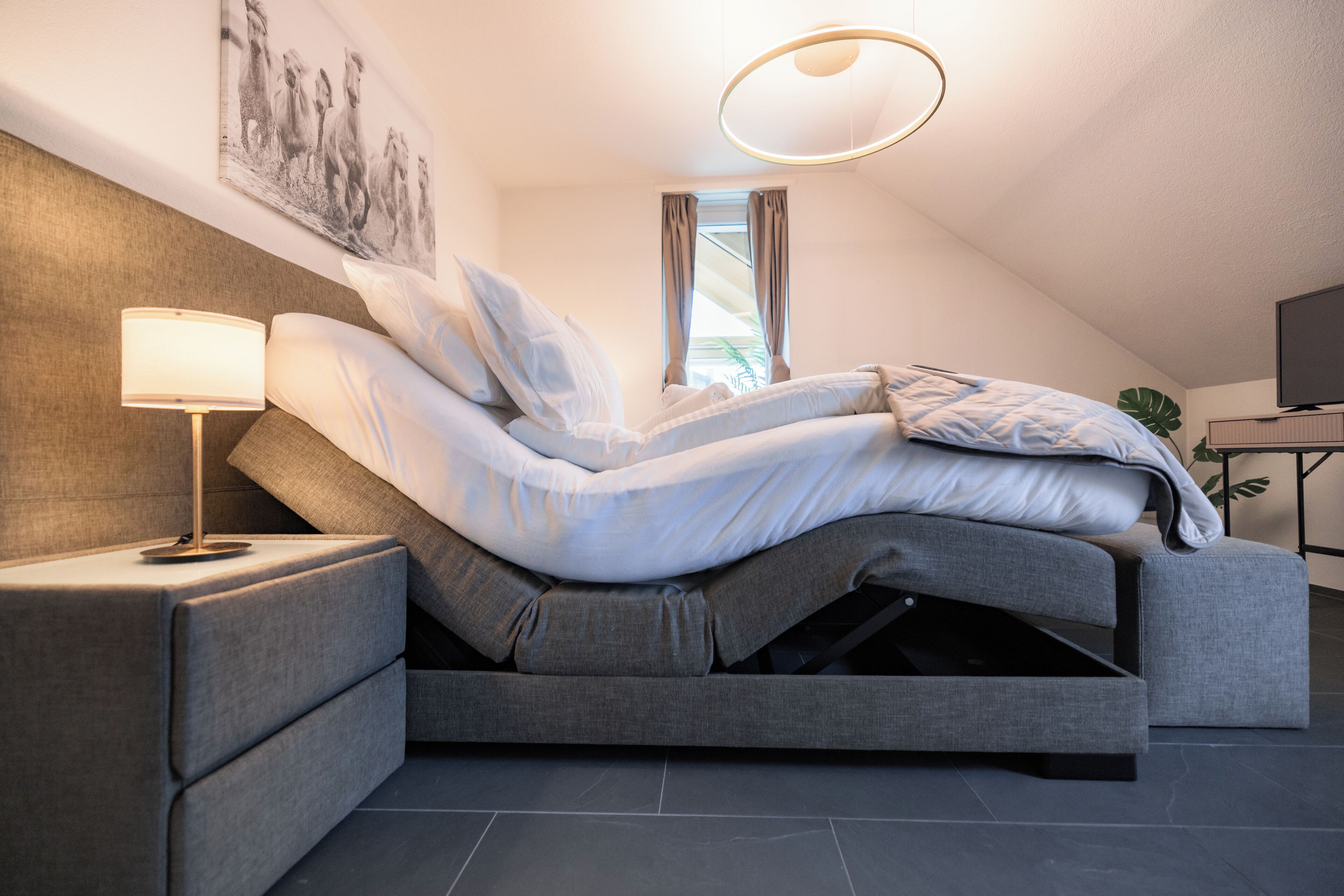 Un dormitorio moderno con cama, mesita de noche, lámpara y un cuadro en la pared.