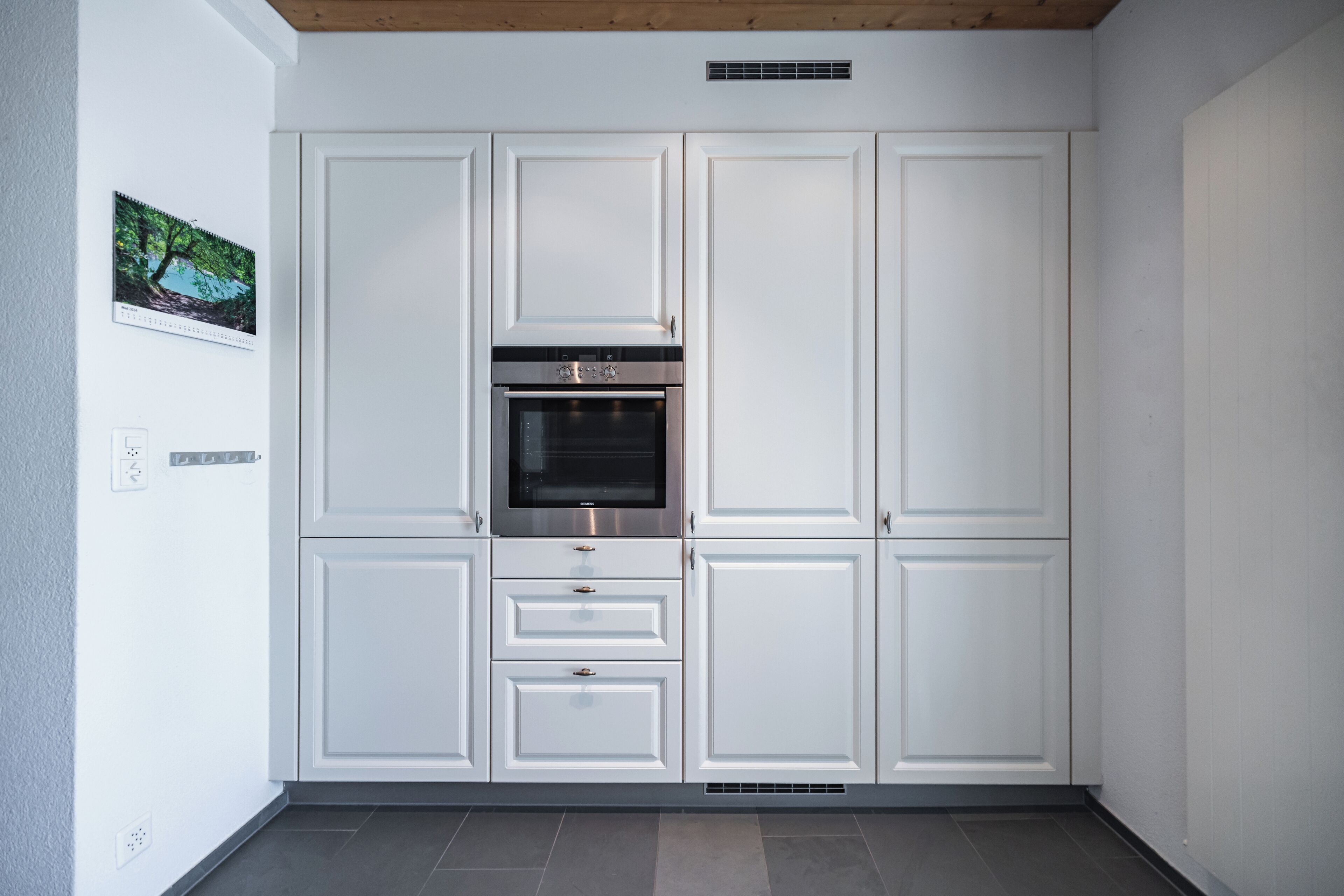 Una cocina con armarios blancos, horno empotrado y extractor en el techo.