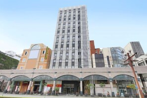 Un edificio de varios pisos con un diseño arquitectónico moderno, que presenta una torre central destacada y una serie de edificios más pequeños con diferentes diseños de fachada.