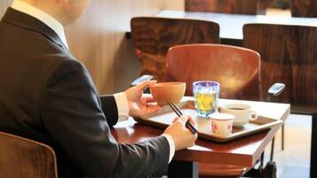A person seated at a table with a bowl, chopsticks, a glass of water, and a cup.