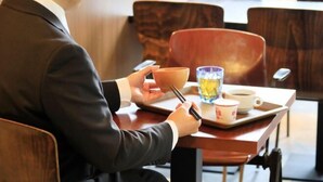 Una persona sentada a una mesa con una taza, un plato y un vaso de agua.