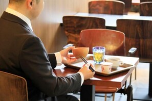 Una persona sentada a una mesa con una taza, un plato y un vaso de agua.