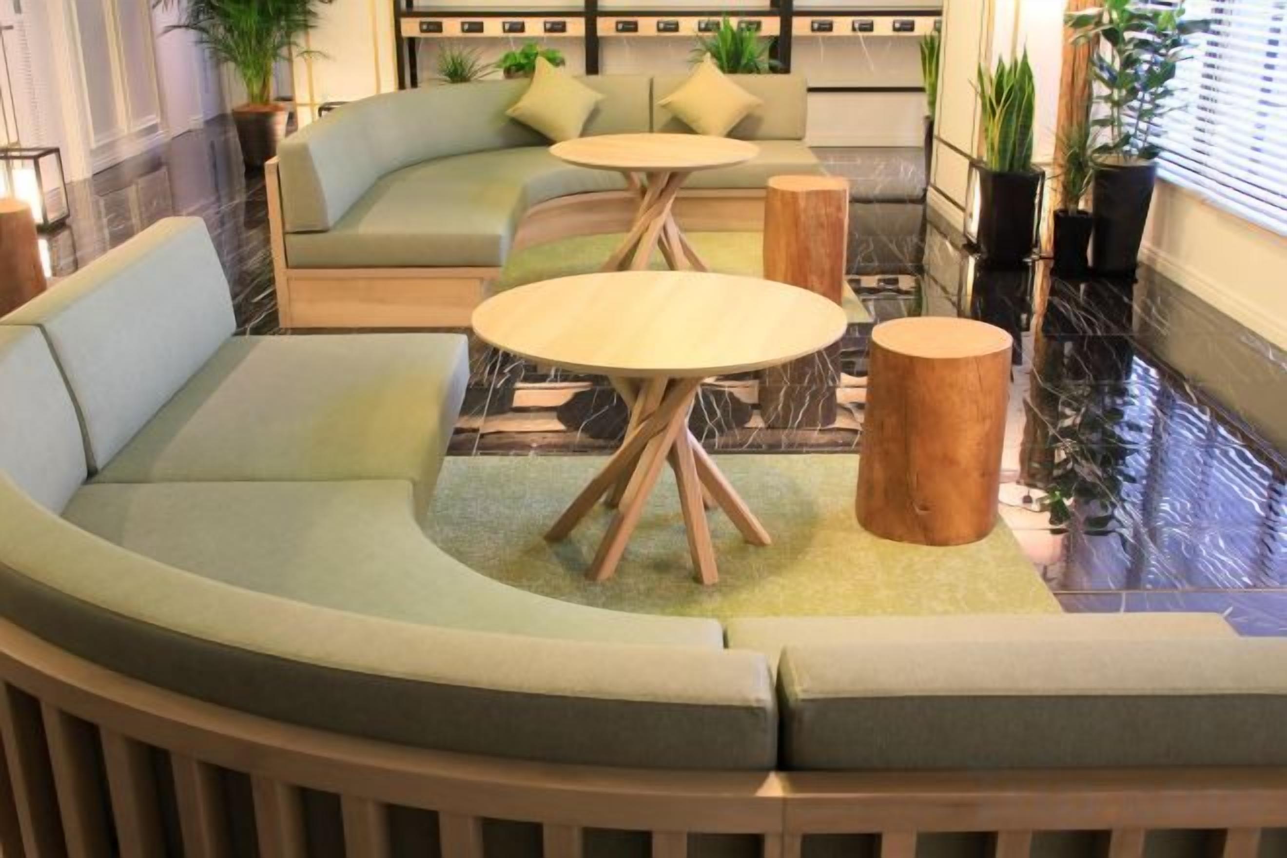 A curved seating area with a sofa and two round tables, a wooden stool, and a potted plant.