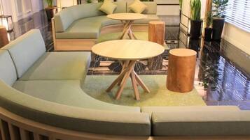 A curved seating area with a sofa and two round tables, a wooden stool, and a potted plant.
