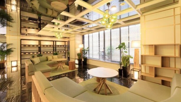 Un área de estar moderna con una mesa redonda central, asientos acolchados y un techo con patrones geométricos y luces colgantes.