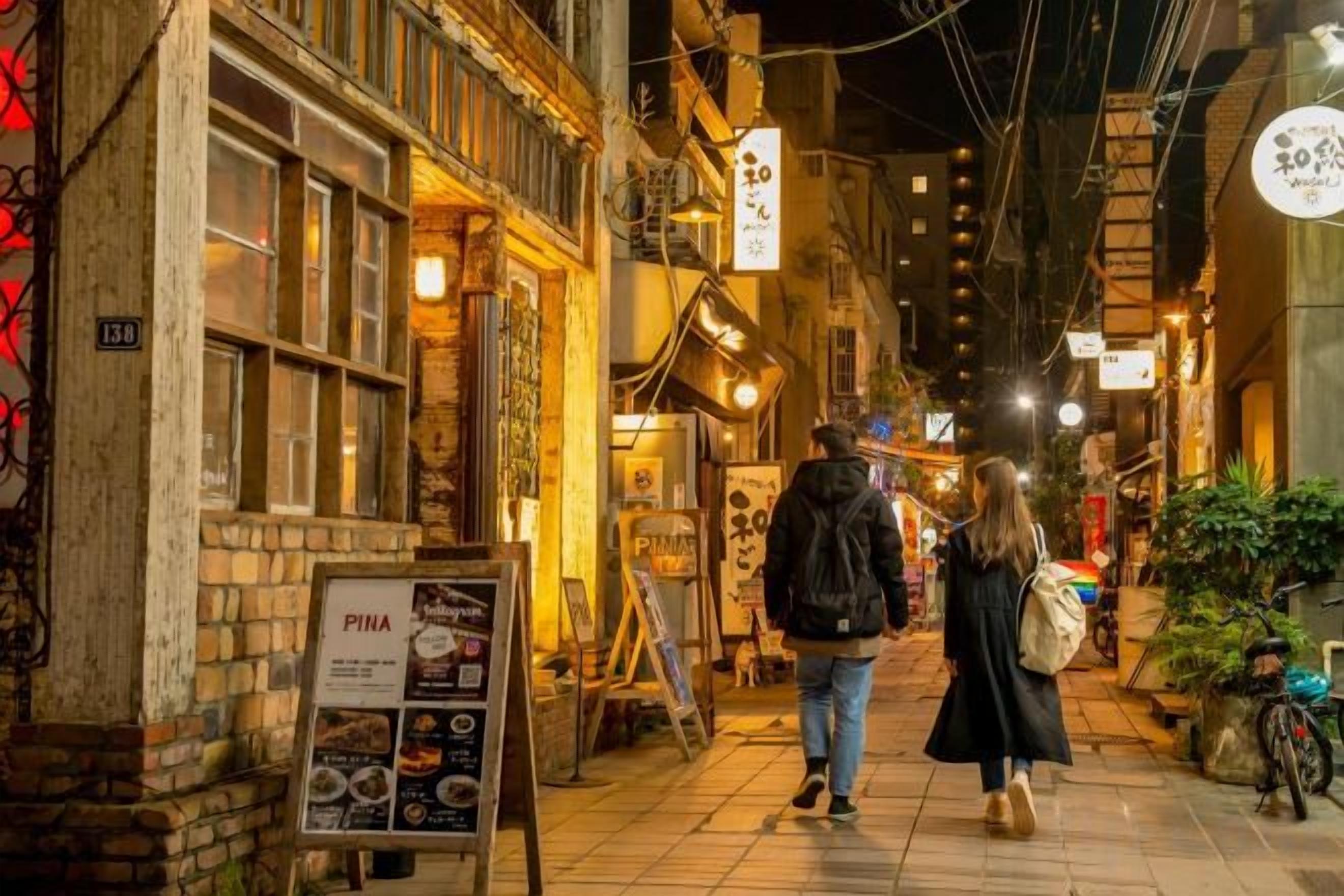 A narrow street with buildings on either side, a signboard, and a person walking.