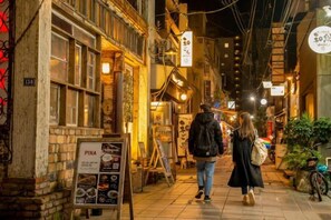 Une rue étroite, bordée de bâtiments des deux côtés, avec une enseigne et une personne qui marche.