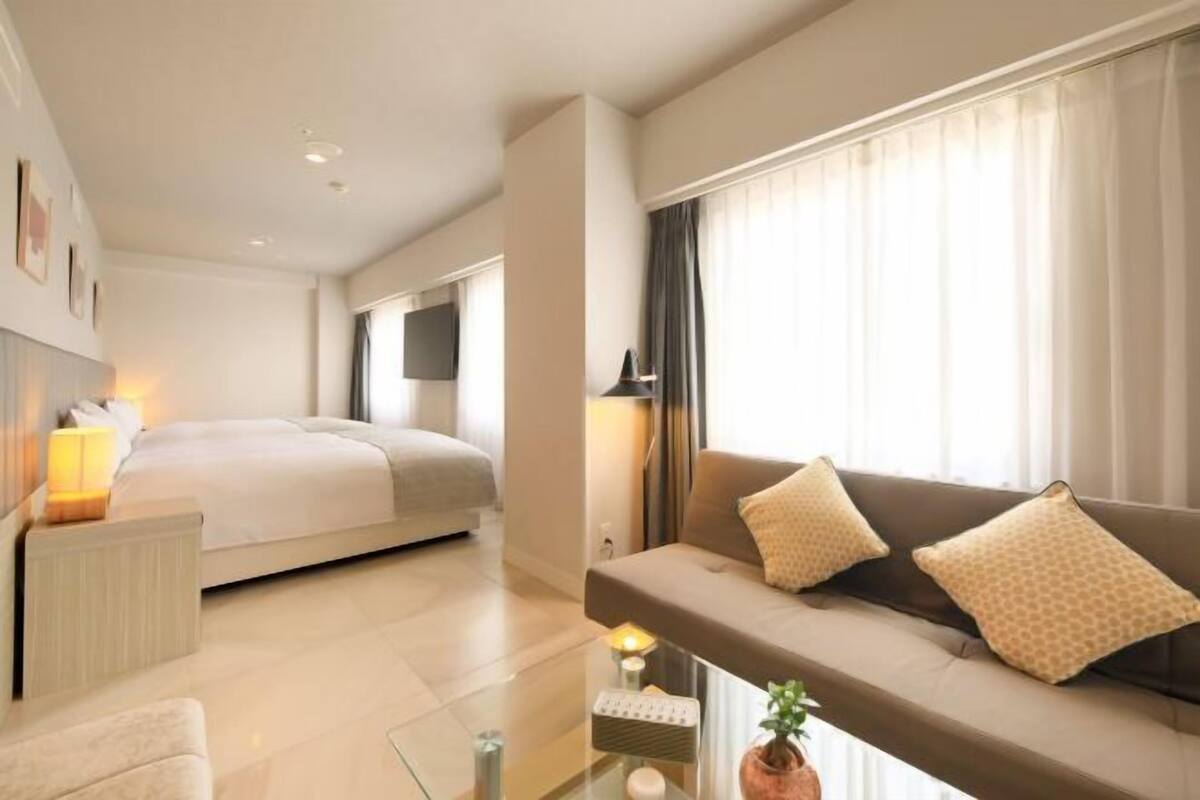 Una habitación de hotel moderna con cama, sofá, mesa de centro y televisión.
