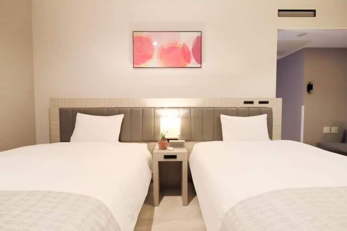 Habitación de hotel con dos camas, una mesita de noche, una obra de arte en la pared y una rejilla en el techo.