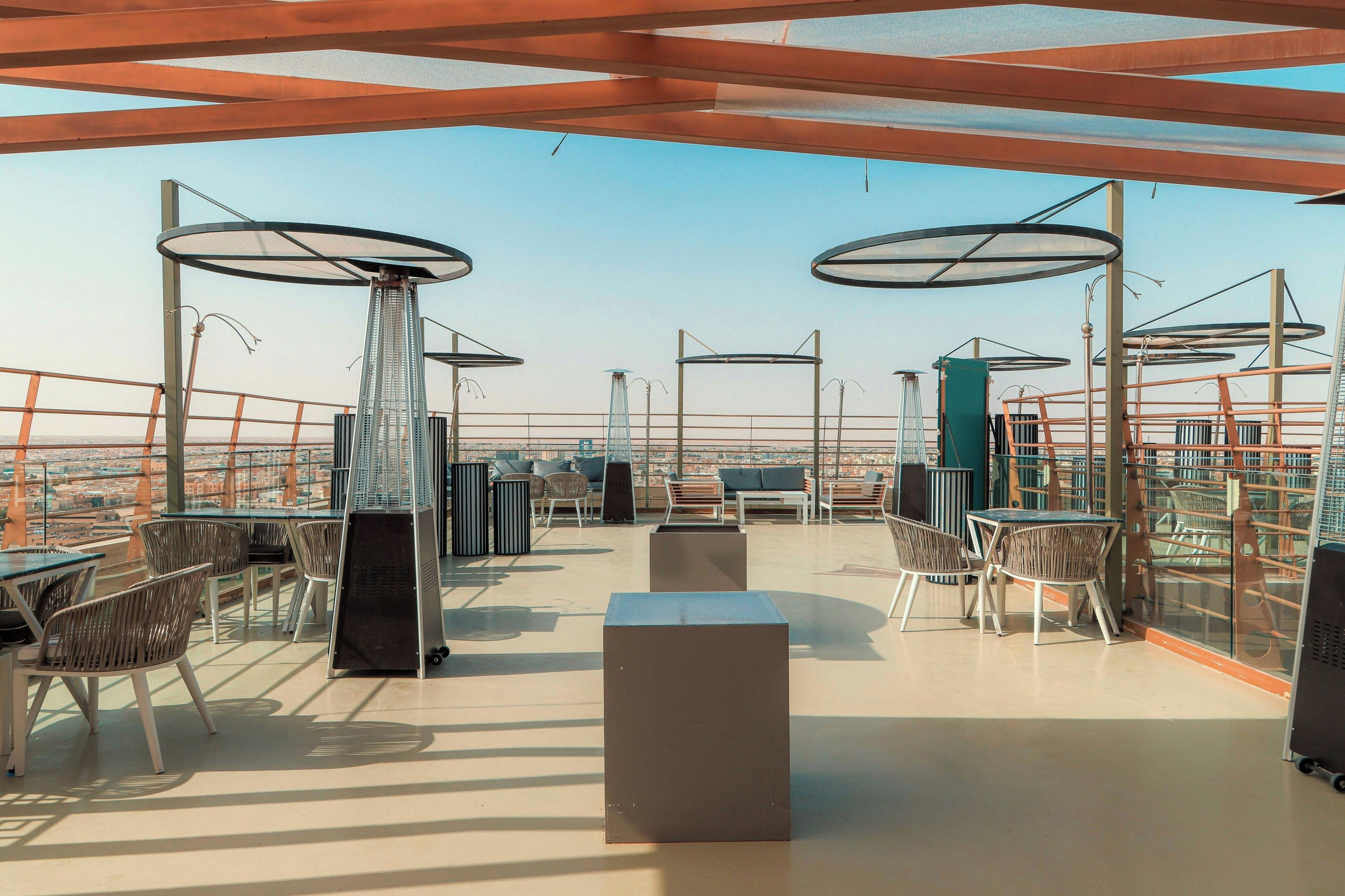 A rooftop terrace with outdoor seating, a view of the cityscape, and a clear sky.