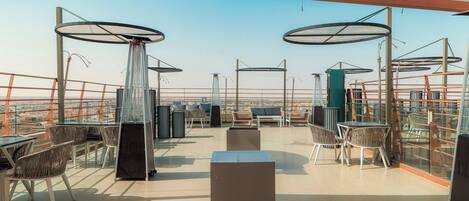A rooftop terrace with outdoor seating, a view of the cityscape, and a clear sky.