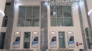 Eine großzügige Lobby mit hohen Decken, großen Fenstern und modernen Möbeln, darunter Sofas und ein Couchtisch.