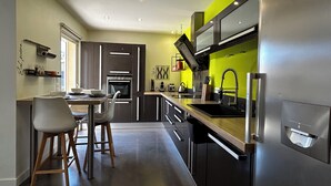 A modern kitchen with a built-in oven, a stainless steel refrigerator, and a wooden dining table with chairs. - Maison Individuelle. Animaux de Compagnie Acceptés (Sainte-Cécile-les-Vignes)
