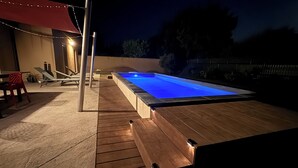 A swimming pool with a wooden deck, lounge chairs, and string lights. - Maison Individuelle. Animaux de Compagnie Acceptés (Sainte-Cécile-les-Vignes)