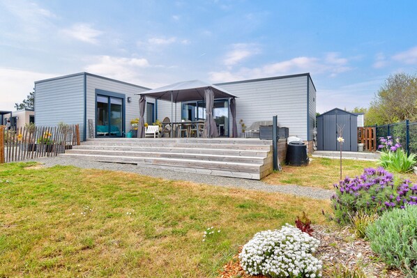 A modern two-story house with a covered patio, a wooden deck, and a garden with various plants.