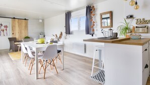 A modern kitchen with a white countertop, a dining area with a white table and chairs, and a window with curtains. - Quiet estate with swimming pool - Chalet for 6 (Bretignolles-sur-Mer)