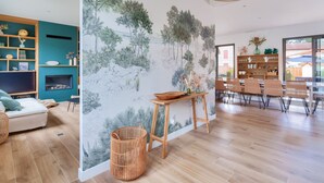 Un salon moderne doté d’un grand téléviseur, d’un canapé et d’un coin repas avec des chaises en osier et une table en bois.