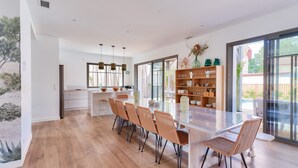 Une cuisine moderne avec une longue table à manger, des chaises en osier et un îlot central doté d’un plateau en verre.