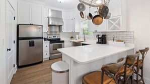 Una cocina moderna con gabinetes blancos, electrodomésticos de acero inoxidable, una isla central con taburetes de bar y ollas colgantes.