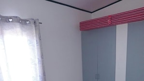 A single bed with a pink bedspread and a floral-patterned blanket, a window with a sheer curtain, and a wall with a vertical stripe pattern. - 3g's & C Calapan Transient House (Calapan)