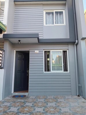 A two-story building with a dark front door, a small window with curtains, and a tiled entrance area. - 3g's & C Calapan Transient House (Calapan)