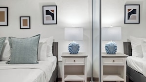 Ein ordentlich eingerichtetes Schlafzimmer mit einem Bett, zwei Nachttischen mit Lampen und gerahmten Bildern an den Wänden.