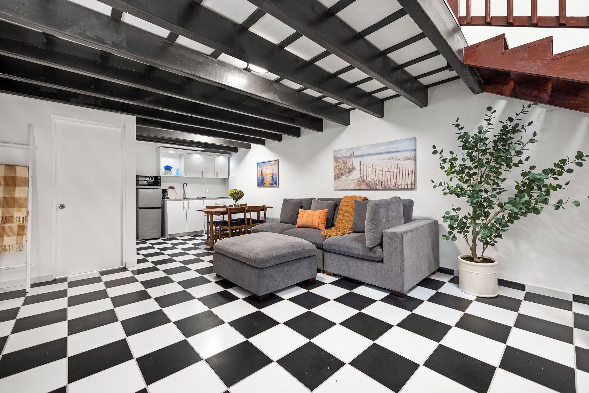 A living room with a checkered floor, a grey sofa, a dining table, and a kitchen in the background.