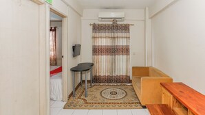 A small, compact room with a sofa, a wooden bench, a small table, a patterned rug, and a curtain. - Hotel O Dms Property (Bekasi)