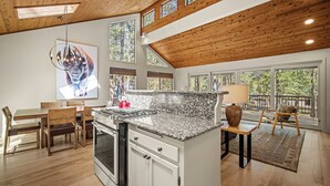 Une cuisine spacieuse dotée d’un grand îlot central, d’un plafond en bois et de grandes fenêtres offrant une vue sur l’extérieur.