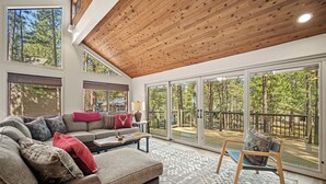 Un salon spacieux avec un grand canapé, une table basse et un fauteuil. Une porte-fenêtre coulissante donne accès à une terrasse extérieure d’où l’on peut admirer la vue sur les arbres.