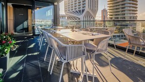 Una terraza moderna en la azotea con zona de comedor, amplias ventanas y vistas a un paisaje urbano.