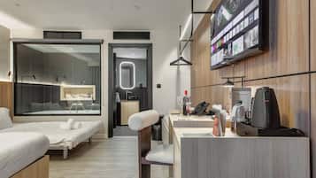 Una habitación de hotel moderna con cama, escritorio con cafetera, televisor y baño con ducha y lavamanos.