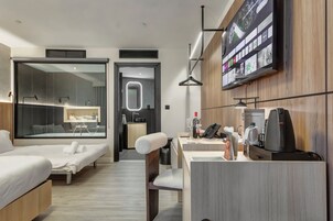 Una habitación de hotel moderna con cama, escritorio con cafetera, televisor y baño con ducha y lavamanos.