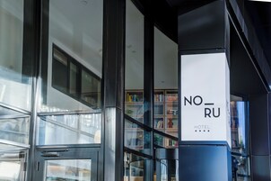 Una entrada de hotel moderna con puerta de vidrio, una escalera visible y una estantería llena de libros.