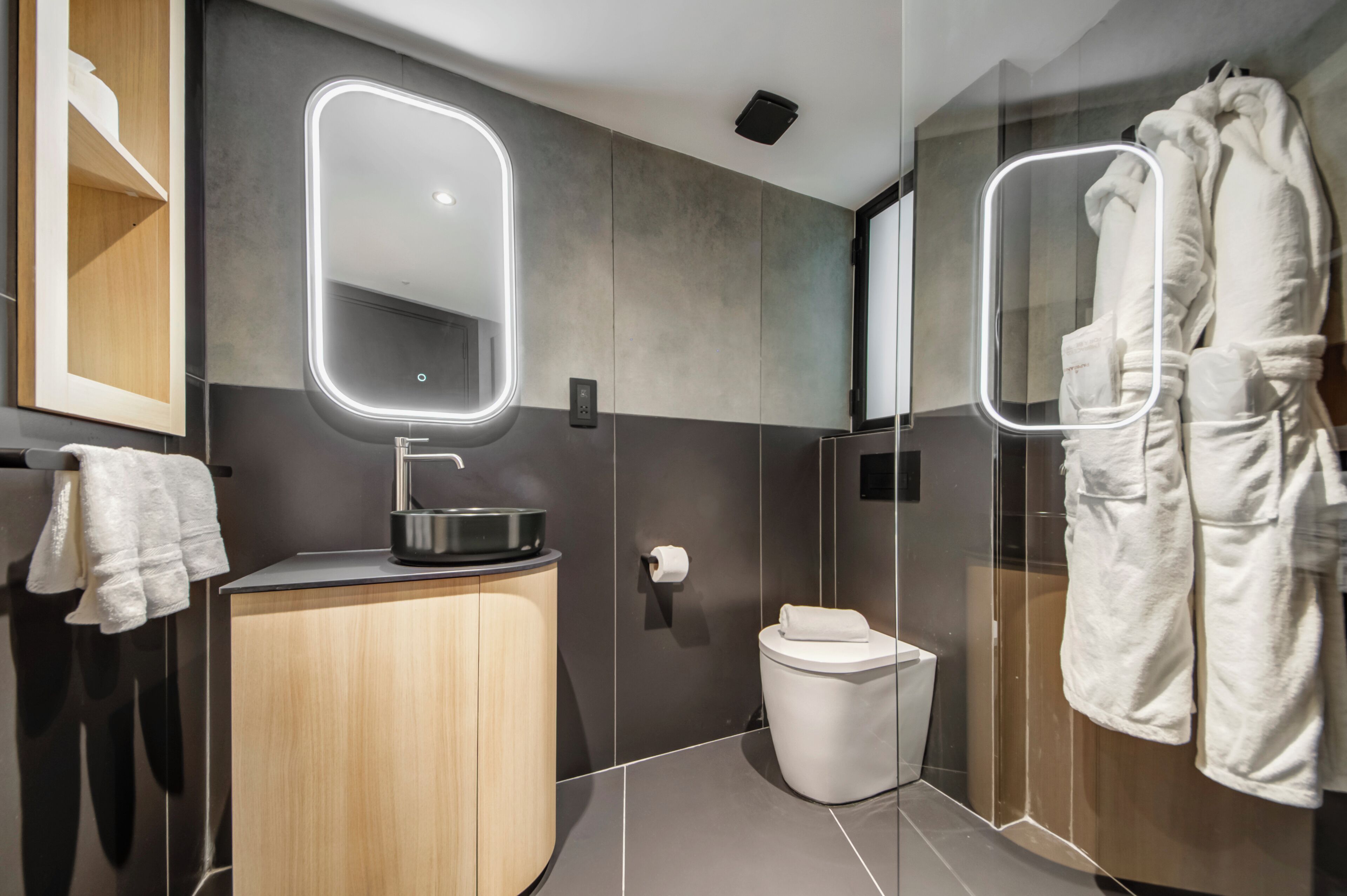 A modern bathroom with a wooden vanity, a glass shower enclosure, and a mirror with built-in lighting.
