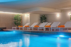 Una piscina con sillas de descanso y cojines anaranjados, rodeada de paredes de madera y plantas.